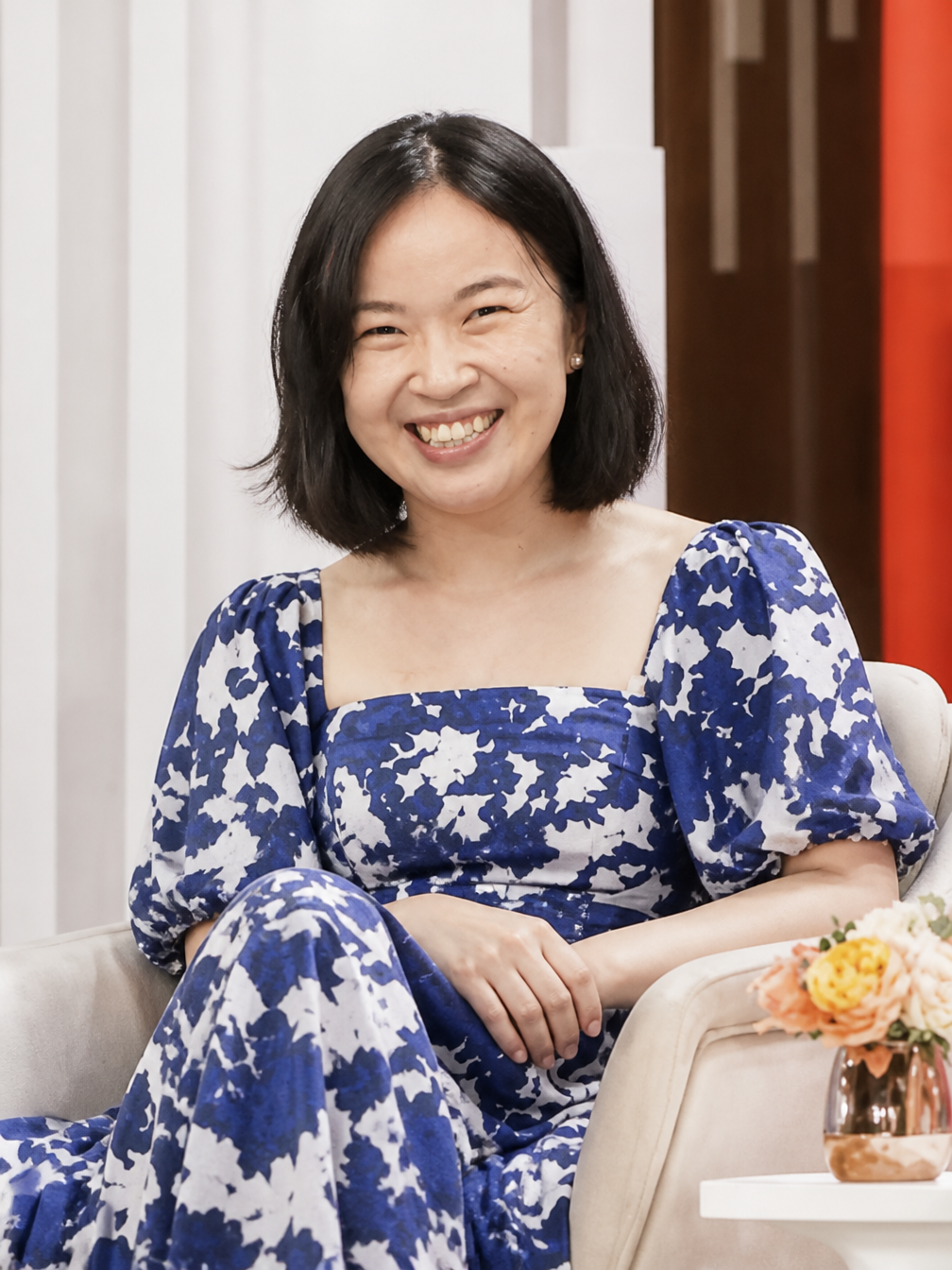 Soh Wan Wei in conversation at a festival fireside — blue floral dress, light backdrop.